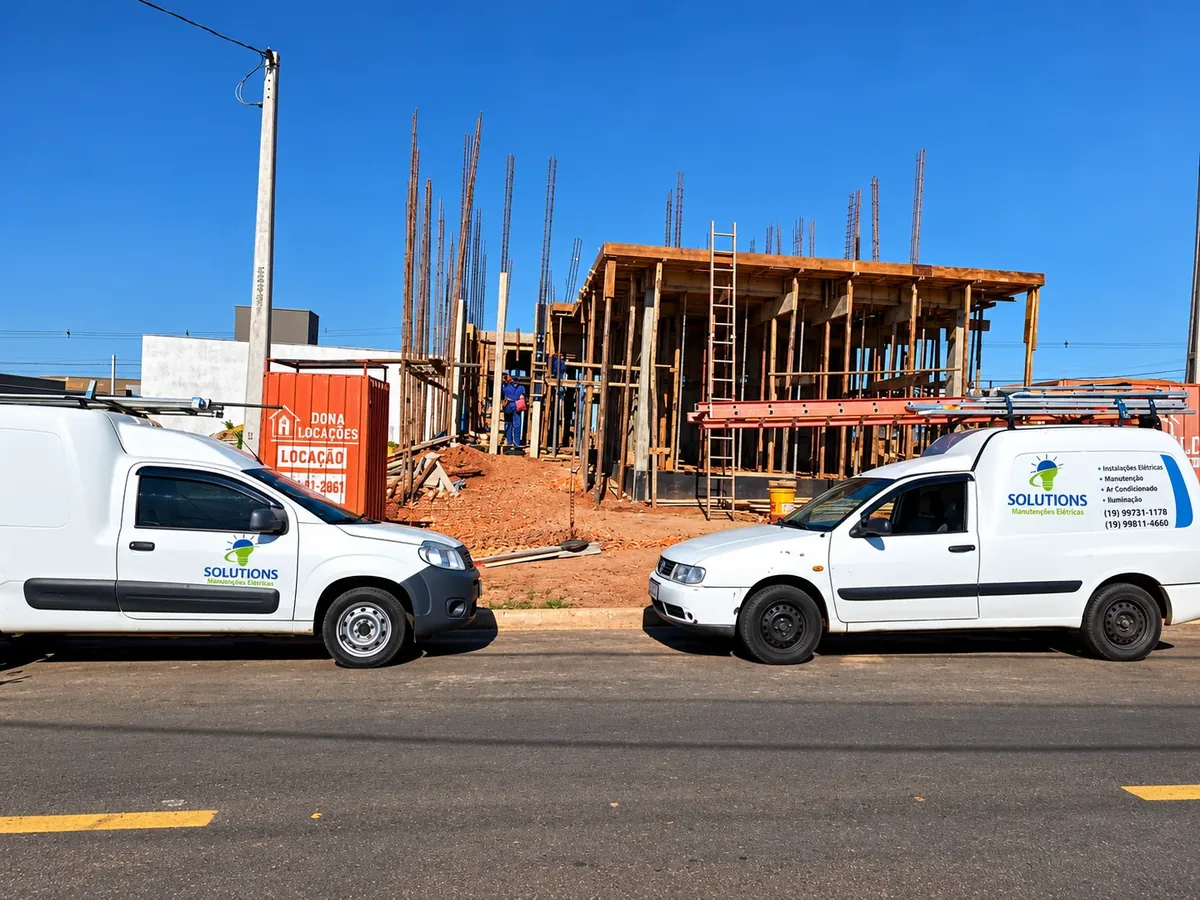 Dois veículos da Solutions estacionados em frente a uma obra, com o logotipo e os telefones da empresa na lateral